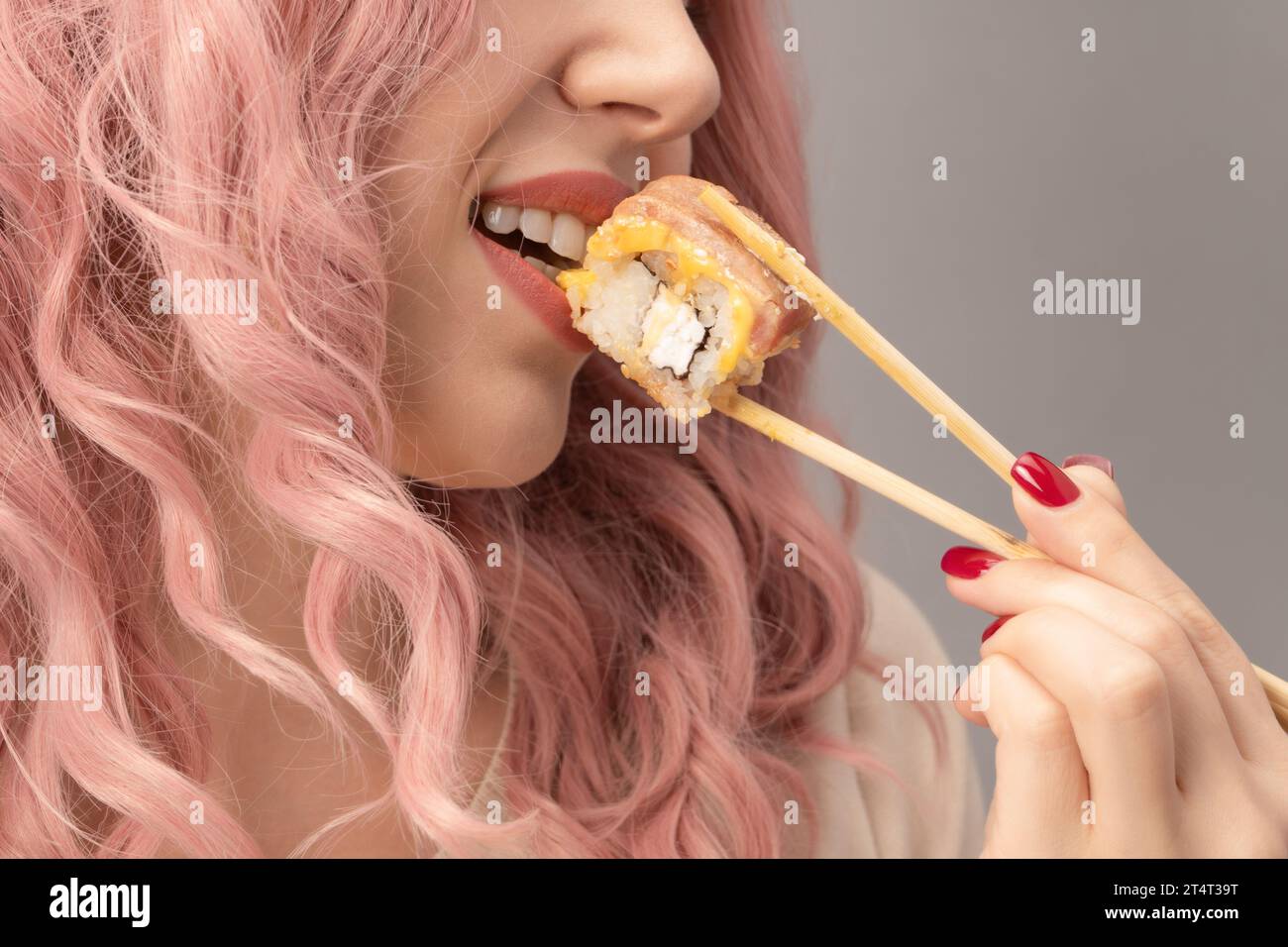 Eine junge Frau mit roten Nägeln und rosa Haaren isst Sushi aus nächster Nähe. Stockfoto