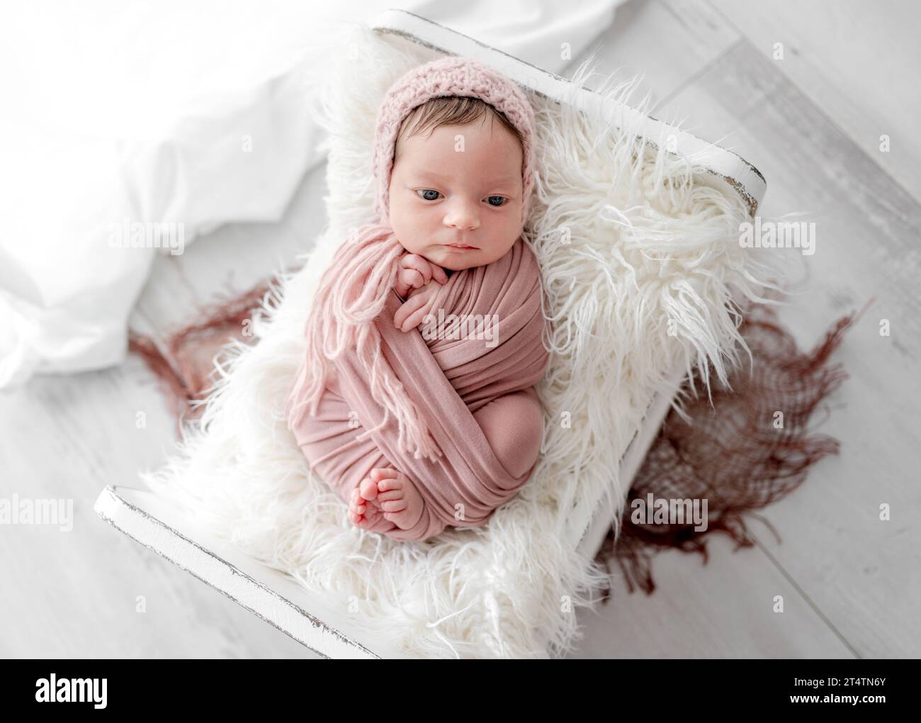 Entzückendes Neugeborenes Mädchen, das in einem winzigen Bett auf einem Pelzporträt liegt. Niedliches Kleinkind, Kind, gewickelt in Stoff, das im Zimmer mit Tageslicht ruht Stockfoto