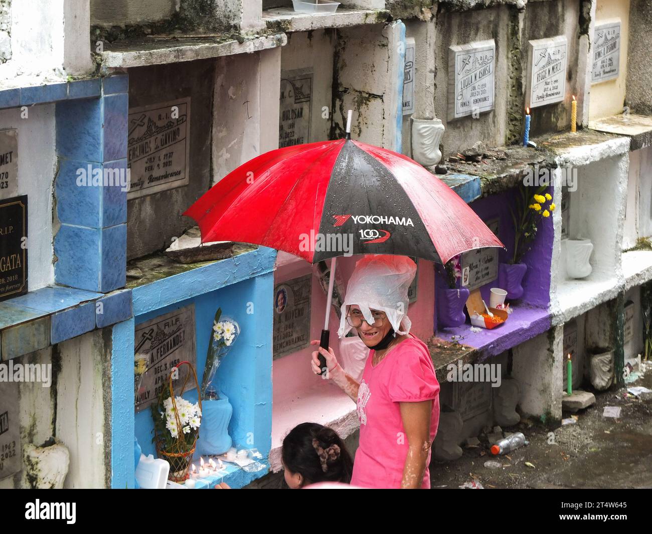 Caloocan, Philippinen. November 2023. Eine alte Frau, die eine Plastiktüte als Kopfbedeckung trägt, um ihr Haar vor Nässe zu schützen, hält einen Regenschirm. Menschen strömen zum Friedhof Sangandaan, um den UNDAS oder Allerheiligen in Caloocan City zu beobachten, trotz heftiger Regenfälle, um ihre verstorbenen Angehörigen zu besuchen. Die Philippine National Police (PNP) Caloocan wurde außerhalb des Friedhofs eingesetzt, um die Ordnung und Sicherheit der Öffentlichkeit zu gewährleisten. Quelle: SOPA Images Limited/Alamy Live News Stockfoto