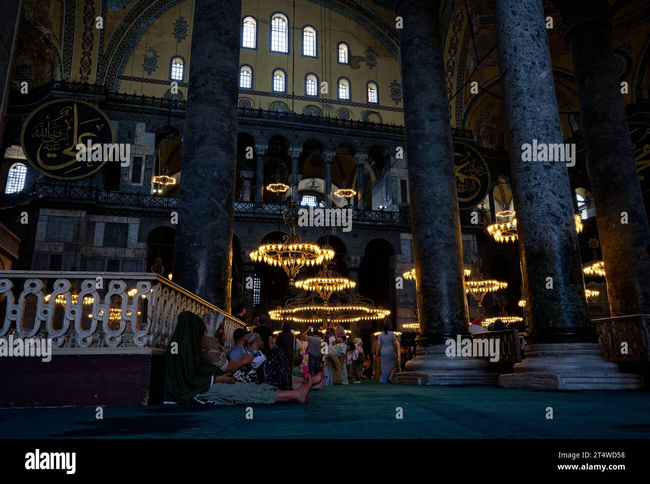 Besucher sitzen, ruhen und beten in der Hagia Sophia, umgeben von Geschichte und Ruhe auf dem emblematischen türkisfarbenen Teppich. Stockfoto