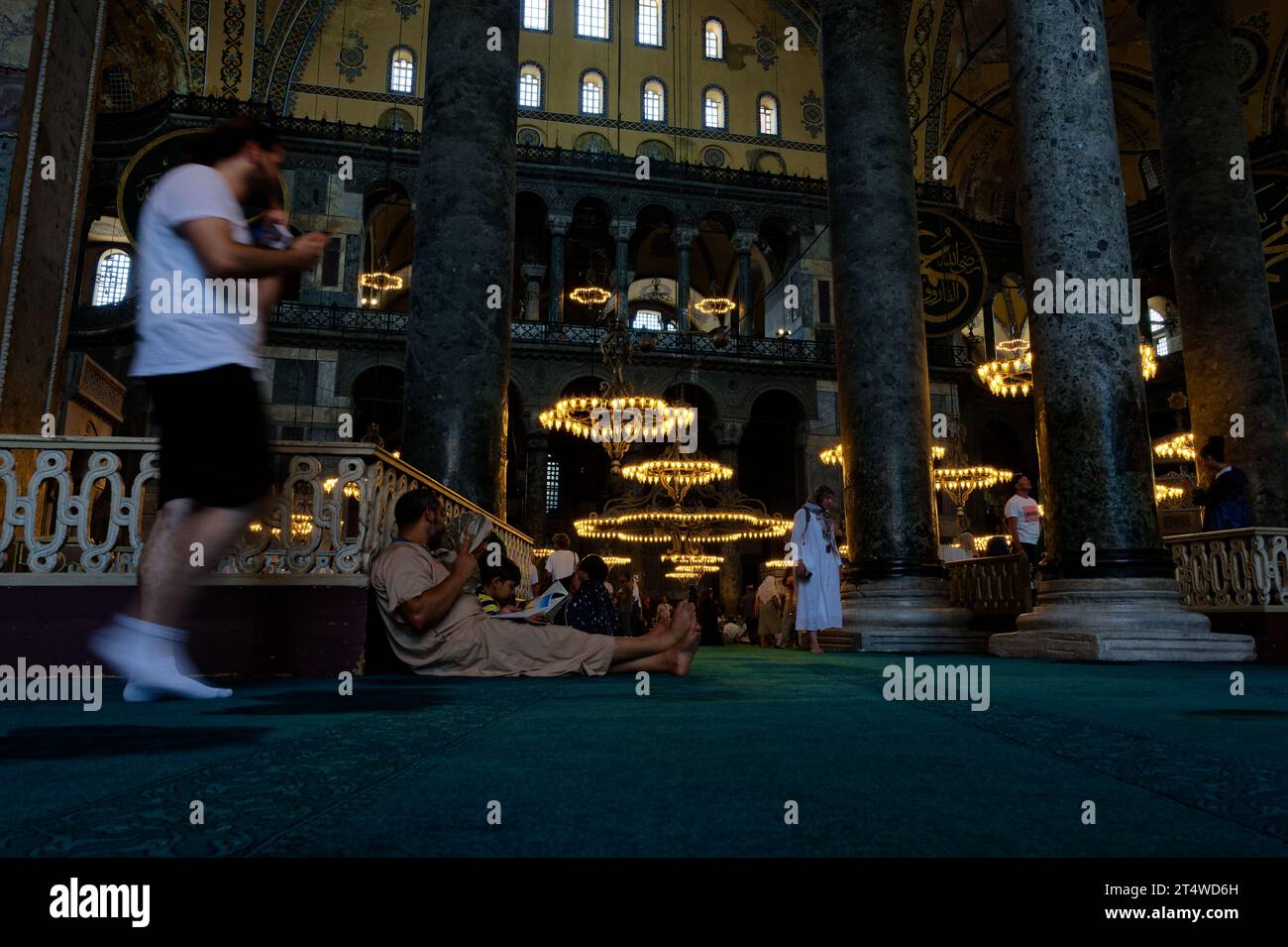 Besucher sitzen, ruhen und beten in der Hagia Sophia, umgeben von Geschichte und Ruhe auf dem emblematischen türkisfarbenen Teppich. Stockfoto
