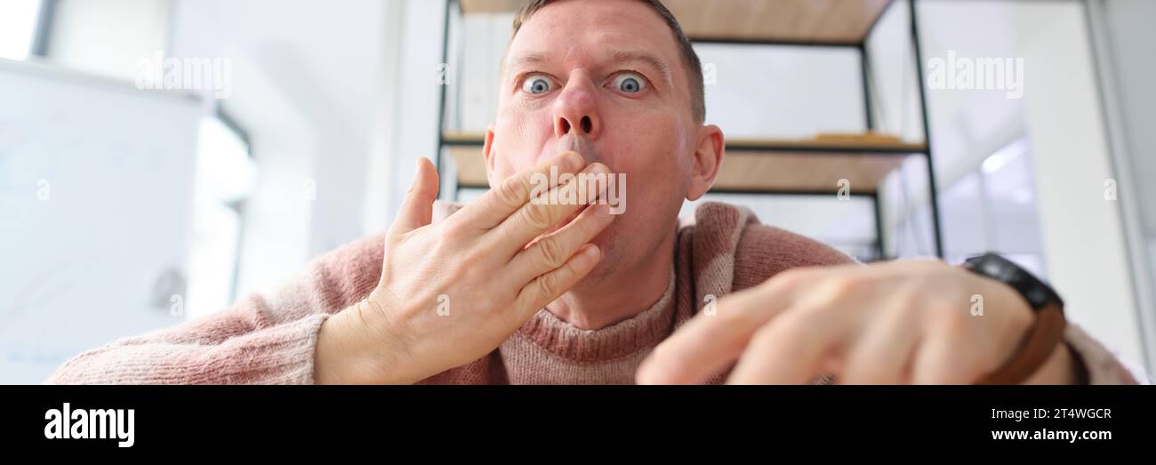 Ein schockierter Mann bedeckt den Mund mit den Augen, die sich die Hand weit öffnen Stockfoto