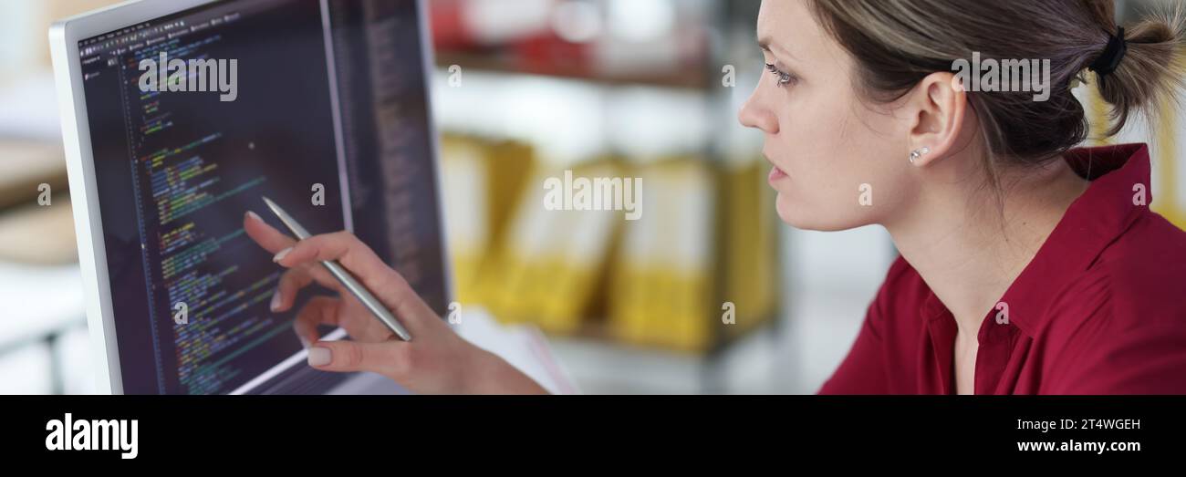 Eine kluge Frau überprüft den Programmcode und zeigt den Stift auf den Bildschirm Stockfoto