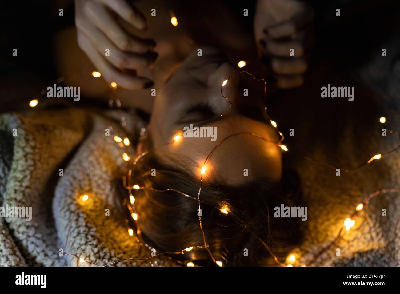 Der Kopf und die Hände einer liegenden Frau mit vielen Weihnachtslichtern Stockfoto