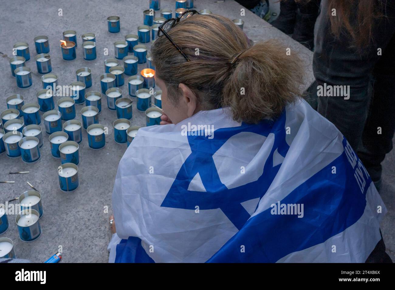 New York, Usa. November 2023. Eine Frau mit einer israelischen Flagge sitzt bei einer Kerzenlicht-Mahnwache für die 1400 Opfer der Terroranschläge der Hamas am 7. Oktober in Israel im Central Park in New York City. Tausende von Zivilisten, sowohl Palästinenser als auch Israelis, sind seit dem 7. Oktober 2023 gestorben, nachdem der im Gazastreifen stationierte palästinensische Hamas-Terrorist in den Süden Israels einmarschierte, bei einem beispiellosen Angriff, der einen von Israel gegen die Hamas erklärten Krieg auslöste. Quelle: SOPA Images Limited/Alamy Live News Stockfoto