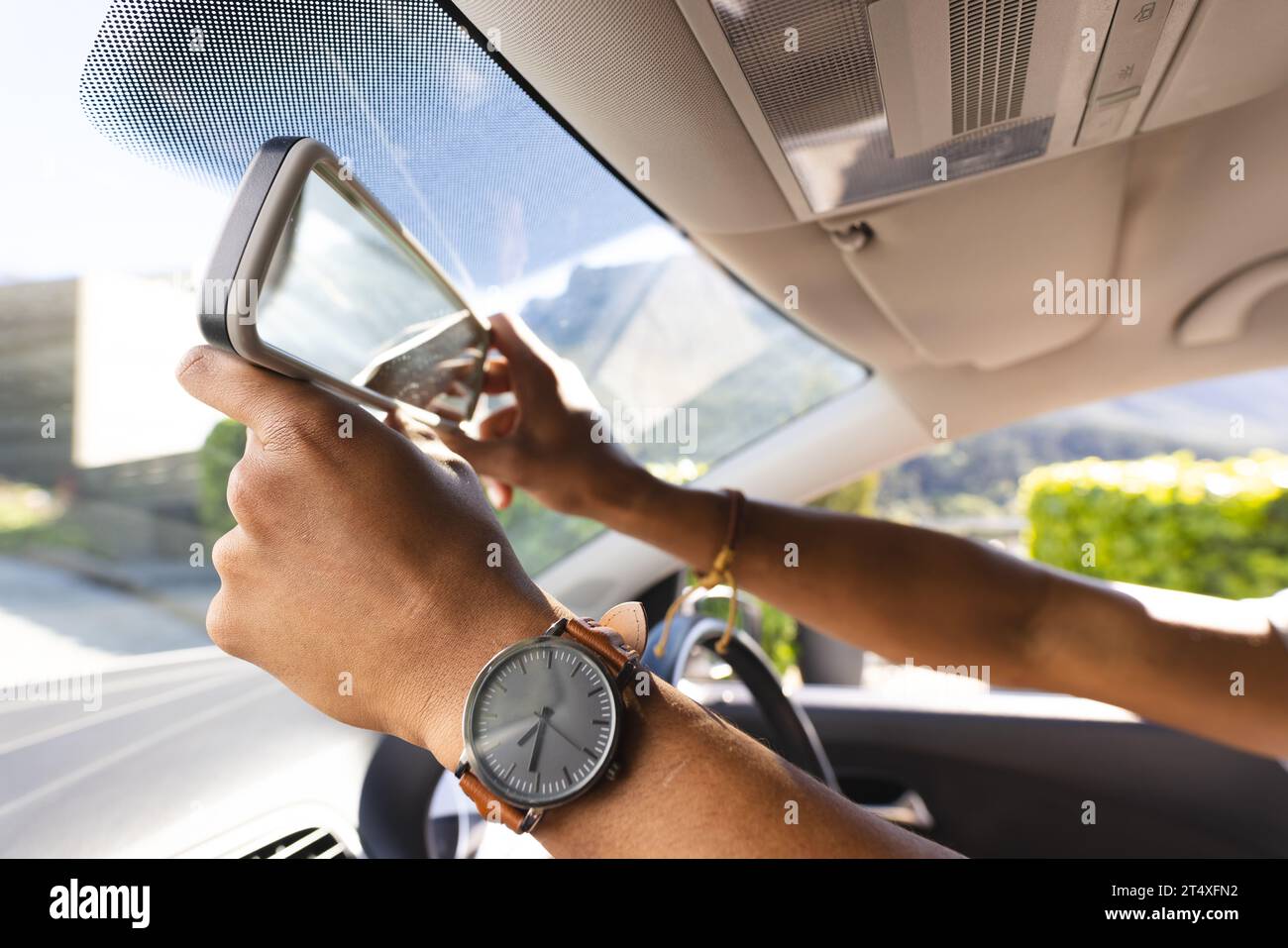 Hände eines afroamerikanischen Mannes, der den Rückspiegel im Auto an sonnigen Tagen justiert Stockfoto