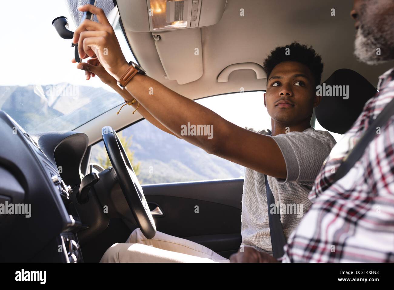 afroamerikanischer erwachsener Sohn, der den Spiegel im Auto während des Fahrunterrichts mit dem Vater verstellt Stockfoto
