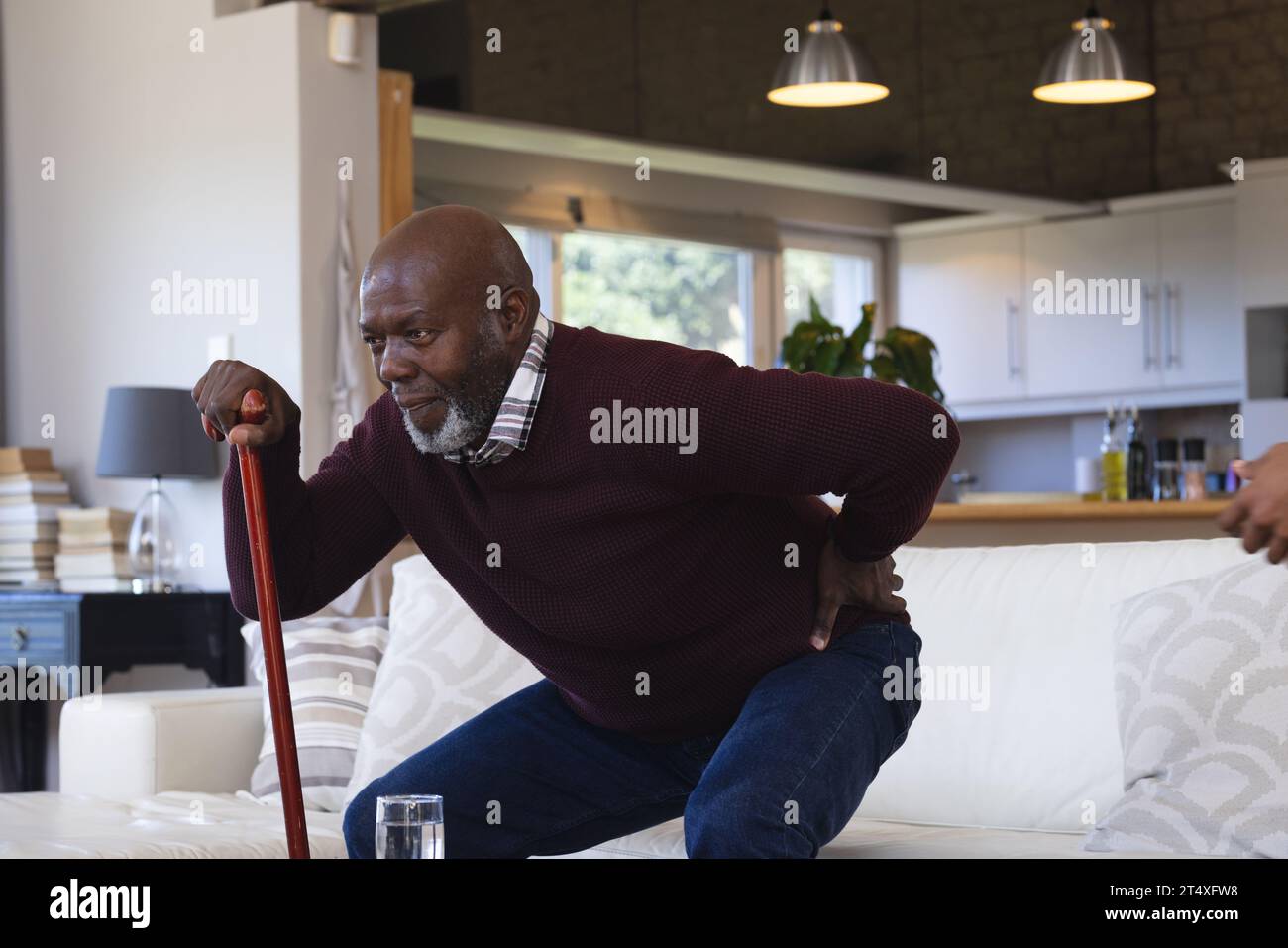 Schmerzhafter afroamerikanischer Senior Mann mit Gehstock, der von der Couch zu Hause aufsteht und sich zurückhält Stockfoto