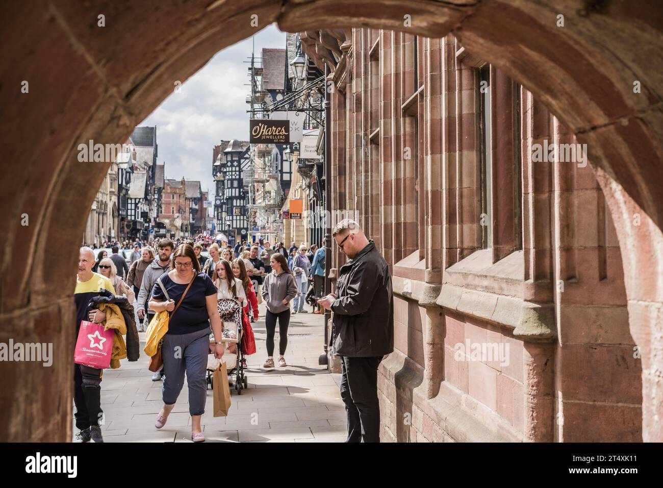 Chester, Cheshire, England, 22. April 2023. Mann, der das Telefon gegen das Gebäude in der belebten traditionellen Innenstadt benutzt, redaktionelle Reise Illustration. Stockfoto