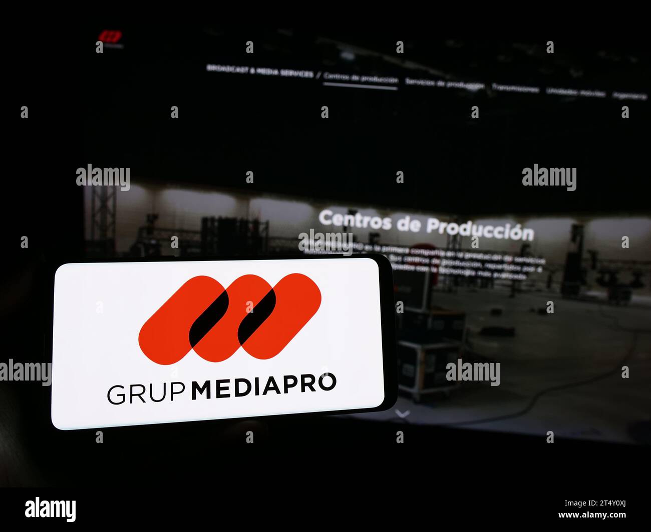Person mit Smartphone und Logo des spanischen Multimedia-Unternehmens Mediapro Group vor der Website. Schwerpunkt auf dem Display des Telefons. Stockfoto