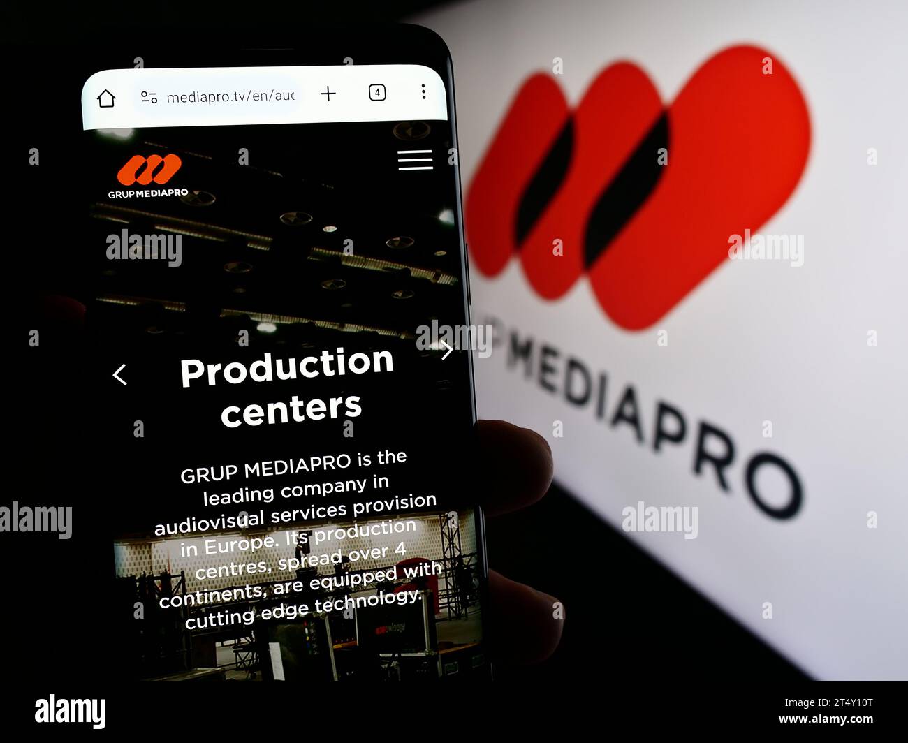 Person, die ein Mobiltelefon hält, mit Webseite des spanischen Multimedia-Unternehmens Mediapro Group vor dem Firmenlogo. Konzentrieren Sie sich auf die Mitte des Telefondisplays. Stockfoto