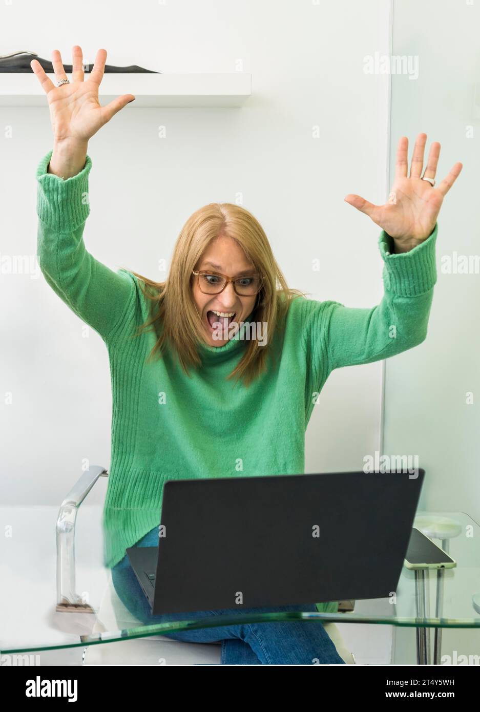 Porträt einer aufgeregten Frau im mittleren Erwachsenenalter, die Erfolge feiert, während sie mit einem Laptop die Hände hochhebt. WIN-Konzept Stockfoto