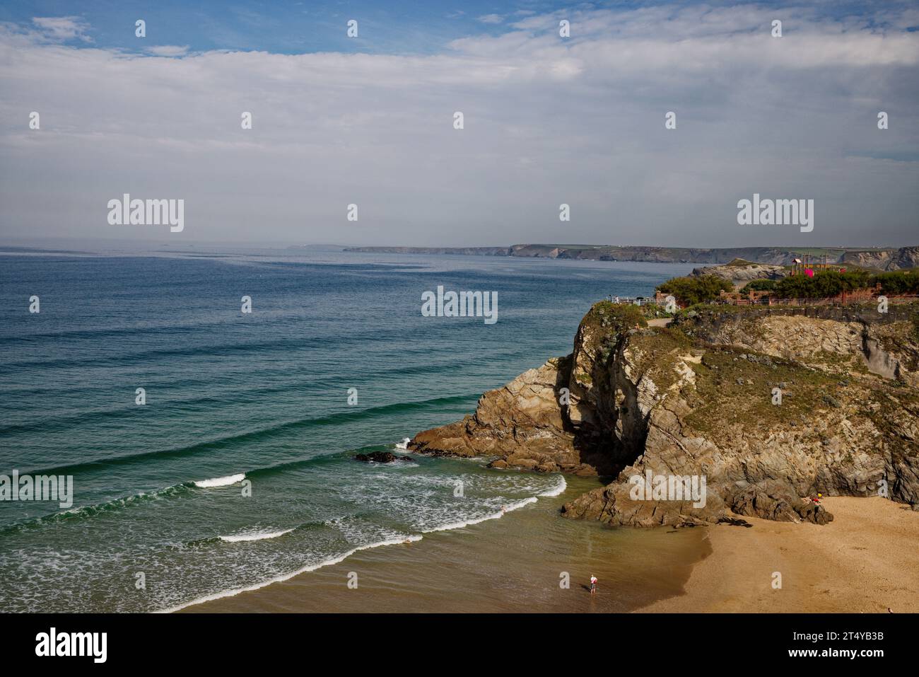 Wellen ziehen sich in eine sandige Bucht von Klippen mit dem blauen Wasser der Newquay Bay dahinter, Cornwall. Stockfoto