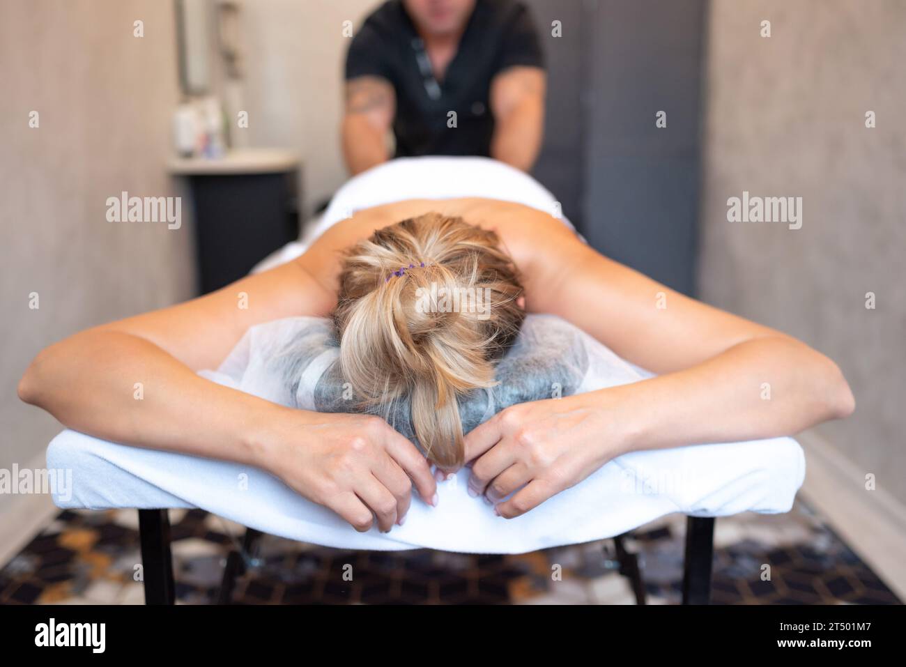 Der männliche Masseur massiert die Rücken- und Schulterblätter der Frau, die auf einem Massagetisch auf hellem Hintergrund liegt. Das Konzept der Massagebehandlungen. Stockfoto