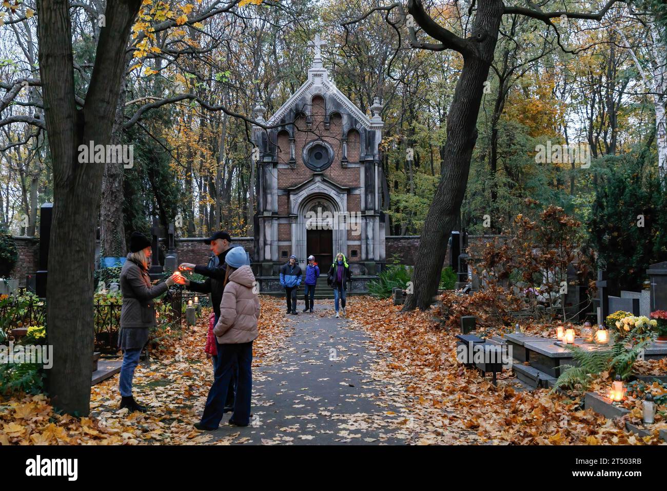 Warschau, Polen. November 2023. Am Allerheiligen-Tag auf dem evangelisch-Augsburger Friedhof in Warschau spazieren die Menschen durch den Friedhof. Allerheiligen (oder Dzie? Zaduszny (Polnisch) ist ein Feiertag in Polen. Es ist eine Gelegenheit, an verstorbene Verwandte zu erinnern. An diesem Tag bringen die Menschen Blumen, typischerweise Chrysanthemen, und Kerzen auf Friedhöfe. Der gesamte Friedhof ist voller Lichter in der Dunkelheit. Der Evangelisch-Augsburger Friedhof ist ein historischer lutherischer evangelischer Friedhof im Westen von Warschau. Seit seiner Eröffnung im Jahr 1792 sind mehr als 100.000 Menschen in buri ansässig Stockfoto