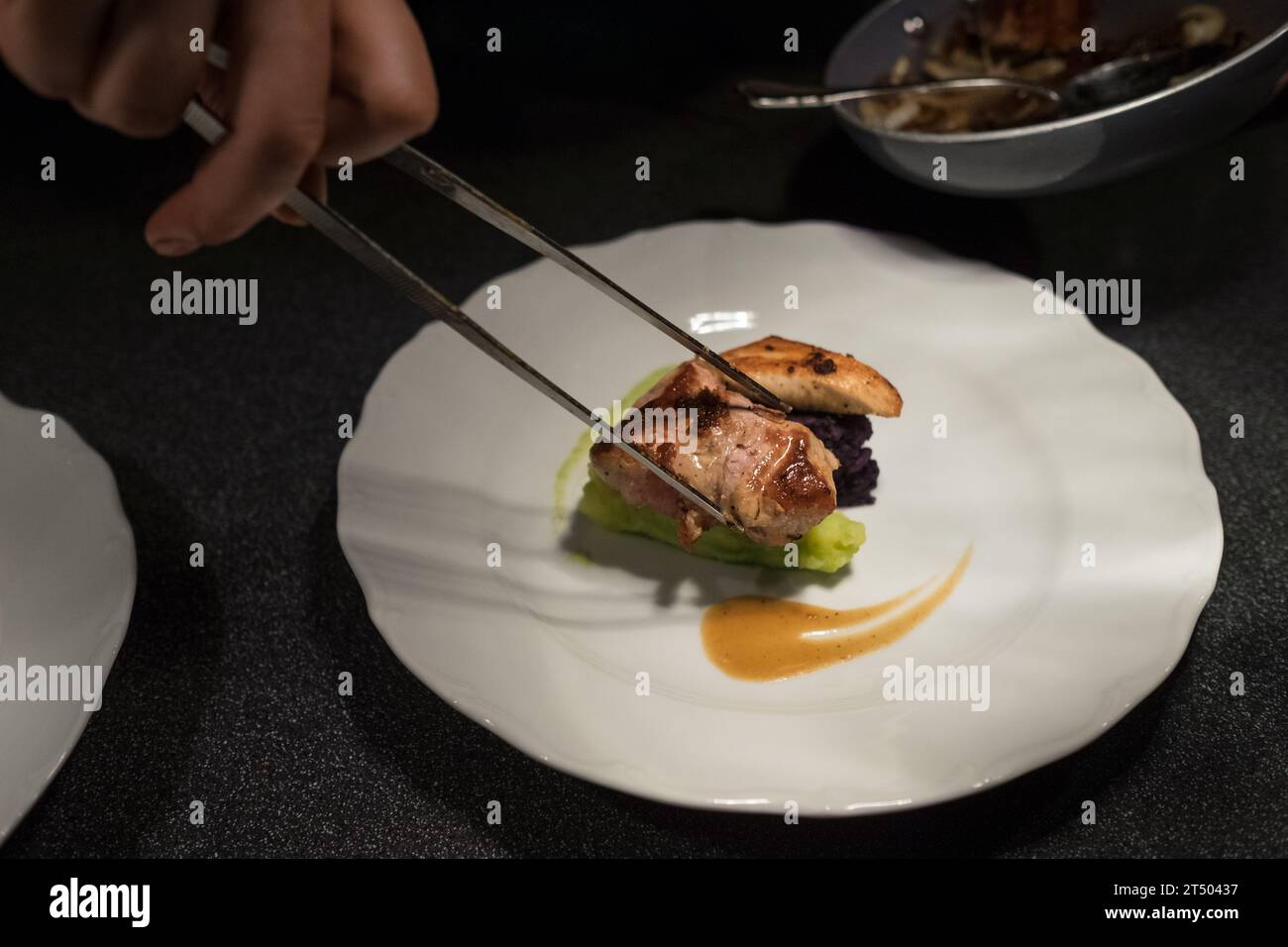 Chef Koch setzen gegrilltes Fleischstück mit einer Pinzette auf grünes Gemüse püriert weißen Teller mit Sauce. Gesunde Mahlzeiten Zubereitung, Kochen oder Kleinbus Stockfoto