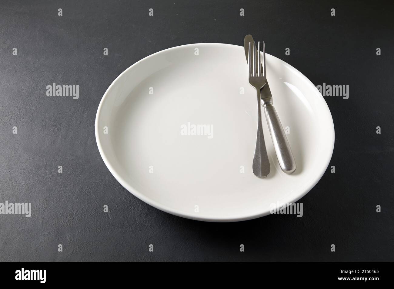 Leere weiße Keramikplatte mit Besteck auf einem schwarzen Steintisch. Vorlage für die Anzeige von Speisen auf dem Menü Stockfoto