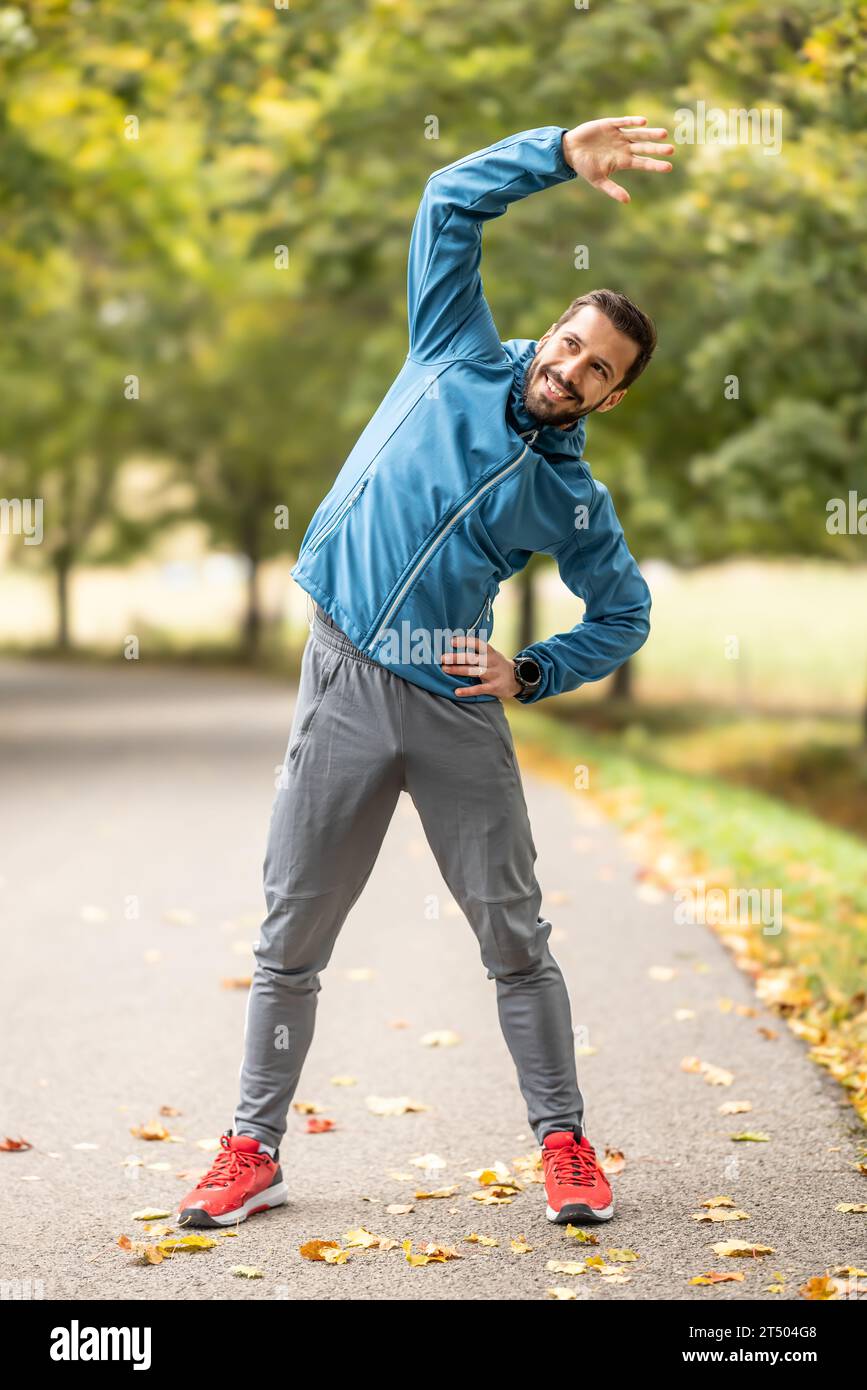 Ein junger Athlet wärmt sich vor dem Lauftraining im Park auf. Sie erwärmt den oberen Teil des Körpers. Stockfoto