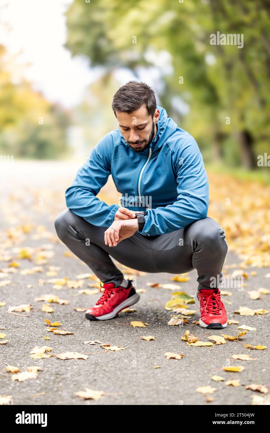 Ein gut aussehender Sportler überprüft die Messwerte auf einer Sportuhr und ruht sich aus. Stockfoto