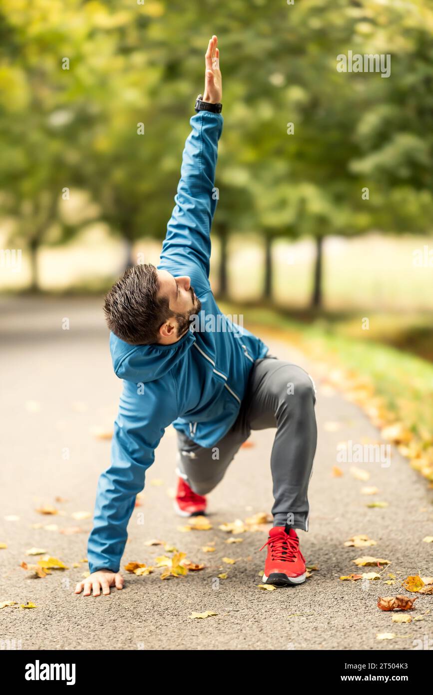 Ein junger Athlet wärmt sich vor dem Lauftraining im Park auf. Sie erwärmt den oberen und unteren Teil des Körpers. Stockfoto