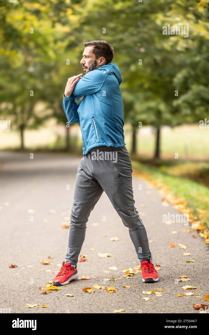 Ein junger Athlet wärmt sich vor dem Lauftraining im Park auf. Sie erwärmt den oberen Teil des Körpers. Stockfoto
