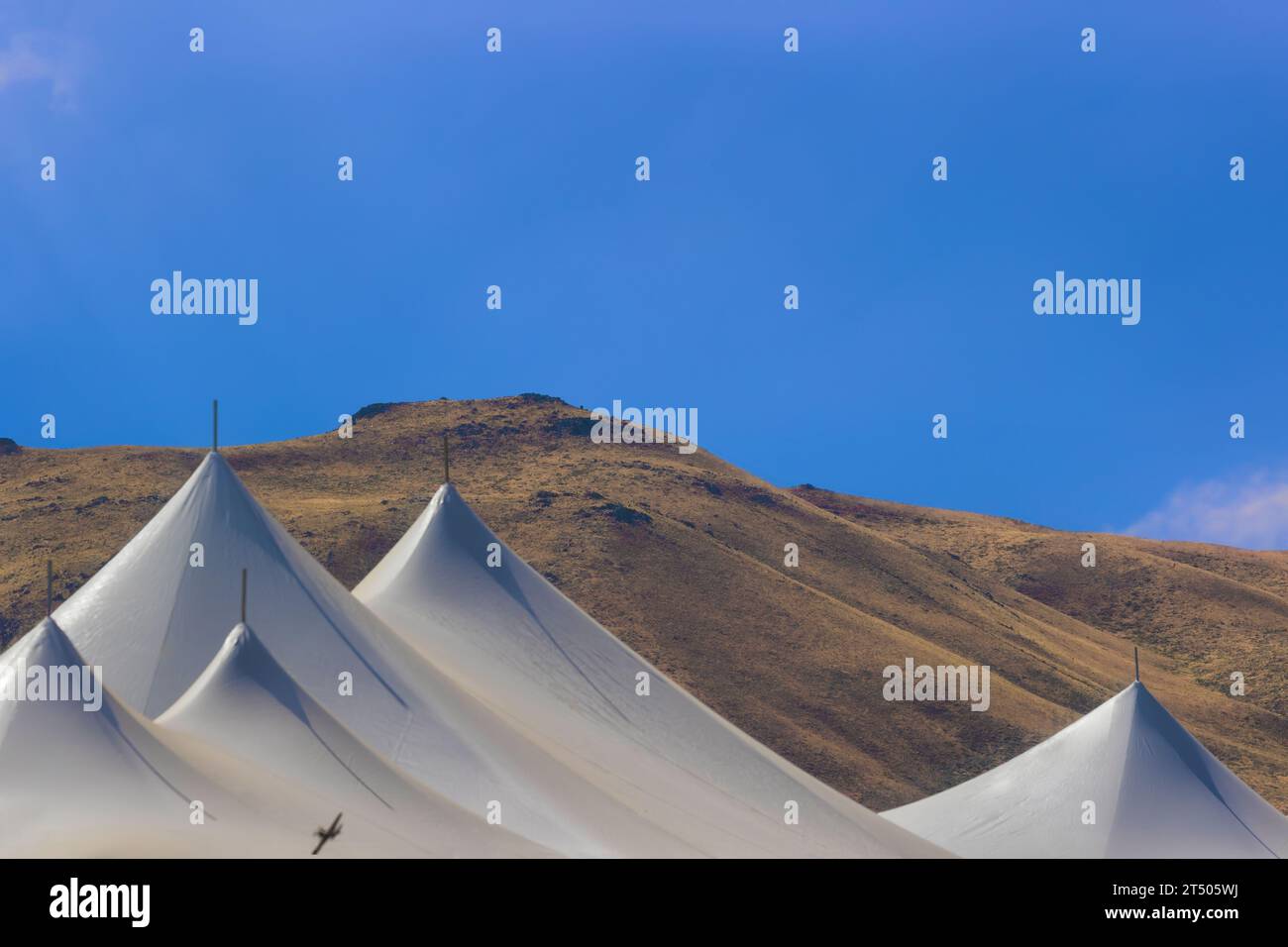 Hochwüstenlandschaft Euter blauer Himmel, Berge und weiße Zeltspitzen, wo man den Schatten eines kleinen Flugzeugs auf dem Zeltdach sehen kann. Stockfoto