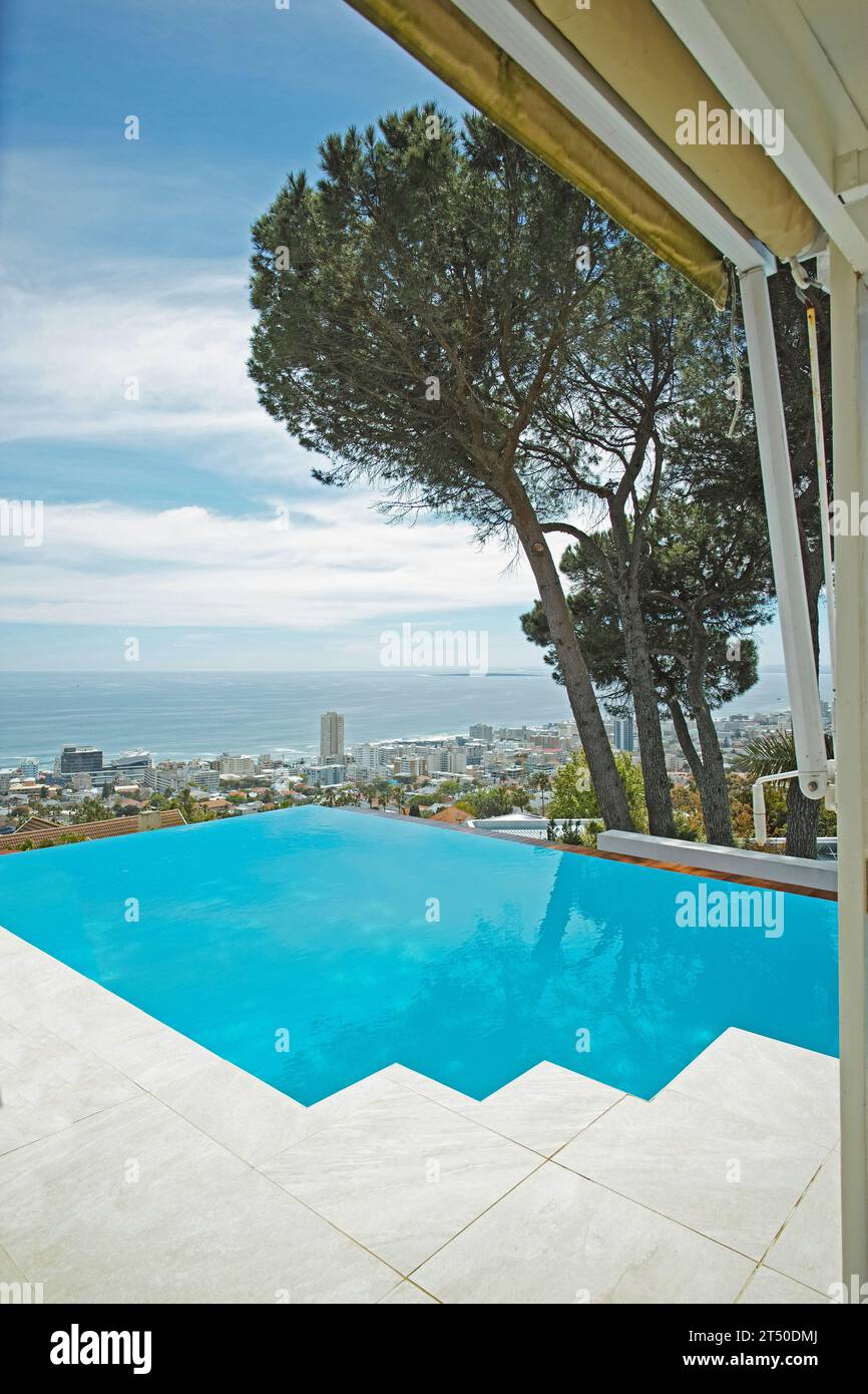 Malerischer Blick auf den Infinity-Swimmingpool mit Blick auf die Stadt und das Meer im Hintergrund. Luxuriöser blauer Außenpool auf einer gefliesten Terrasse, Terrasse und Veranda einer Ferienwohnung Stockfoto