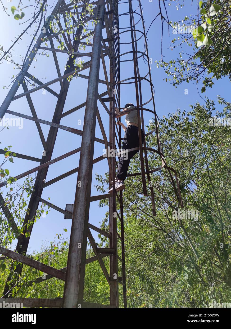 Teenager-Mädchen, das ohne Sicherheitsnetz auf einen verlassenen rostigen Metallturm klettert, Stockfoto