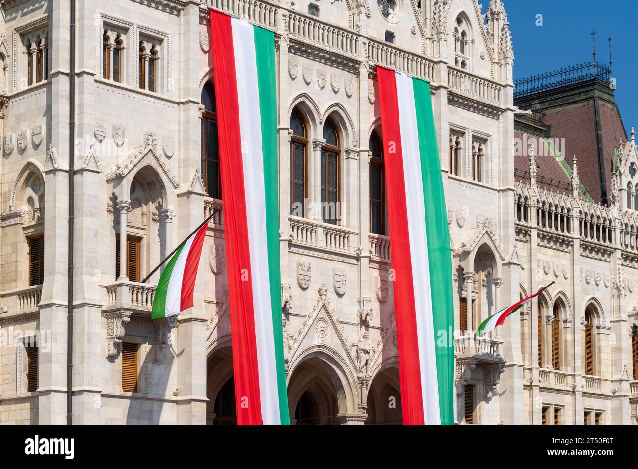 Das neogotische Gebäude des ungarischen Parlaments, das Parlament, ist an einem Nationalfeiertag mit Fahnen in ungarischen Nationalfarben verziert Stockfoto
