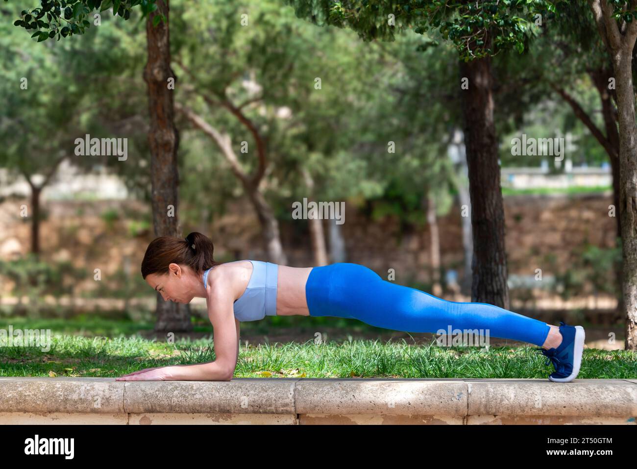 Sportliche Frau, die im Park Planks und Liegestützübungen macht Stockfoto