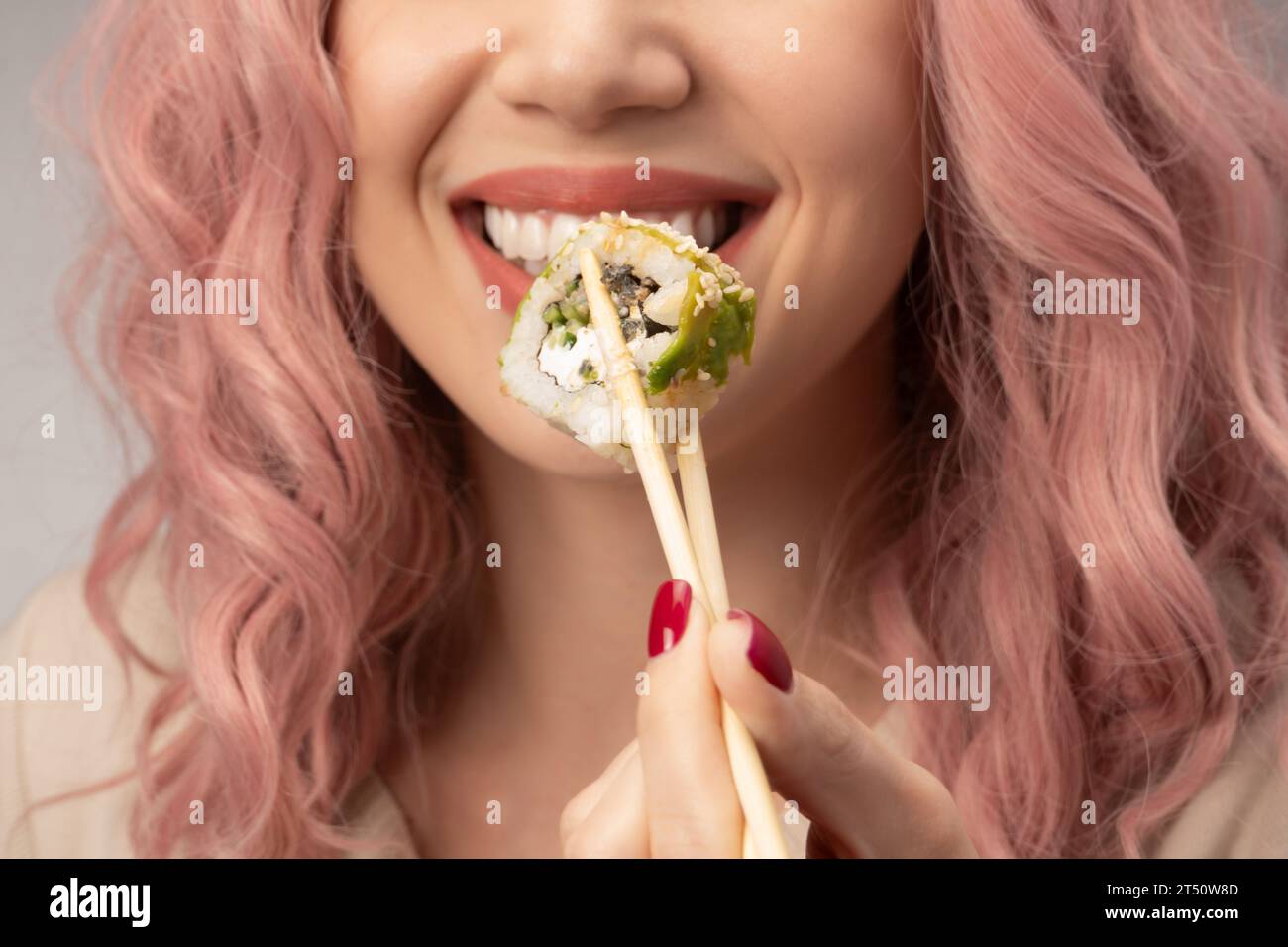 Eine junge Frau mit roten Nägeln und rosa Haaren isst Sushi aus nächster Nähe. Stockfoto