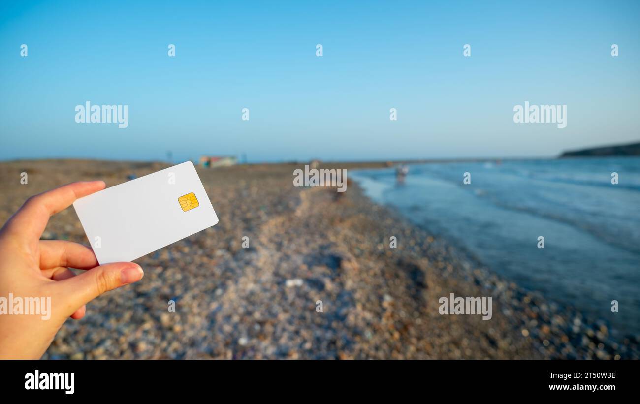 Frau hält weiße Bankkarte in der Hand vor dem Hintergrund eines endlosen Strandes als Symbol für grenzenlose Möglichkeiten und Reisen. Kopierbereich Stockfoto