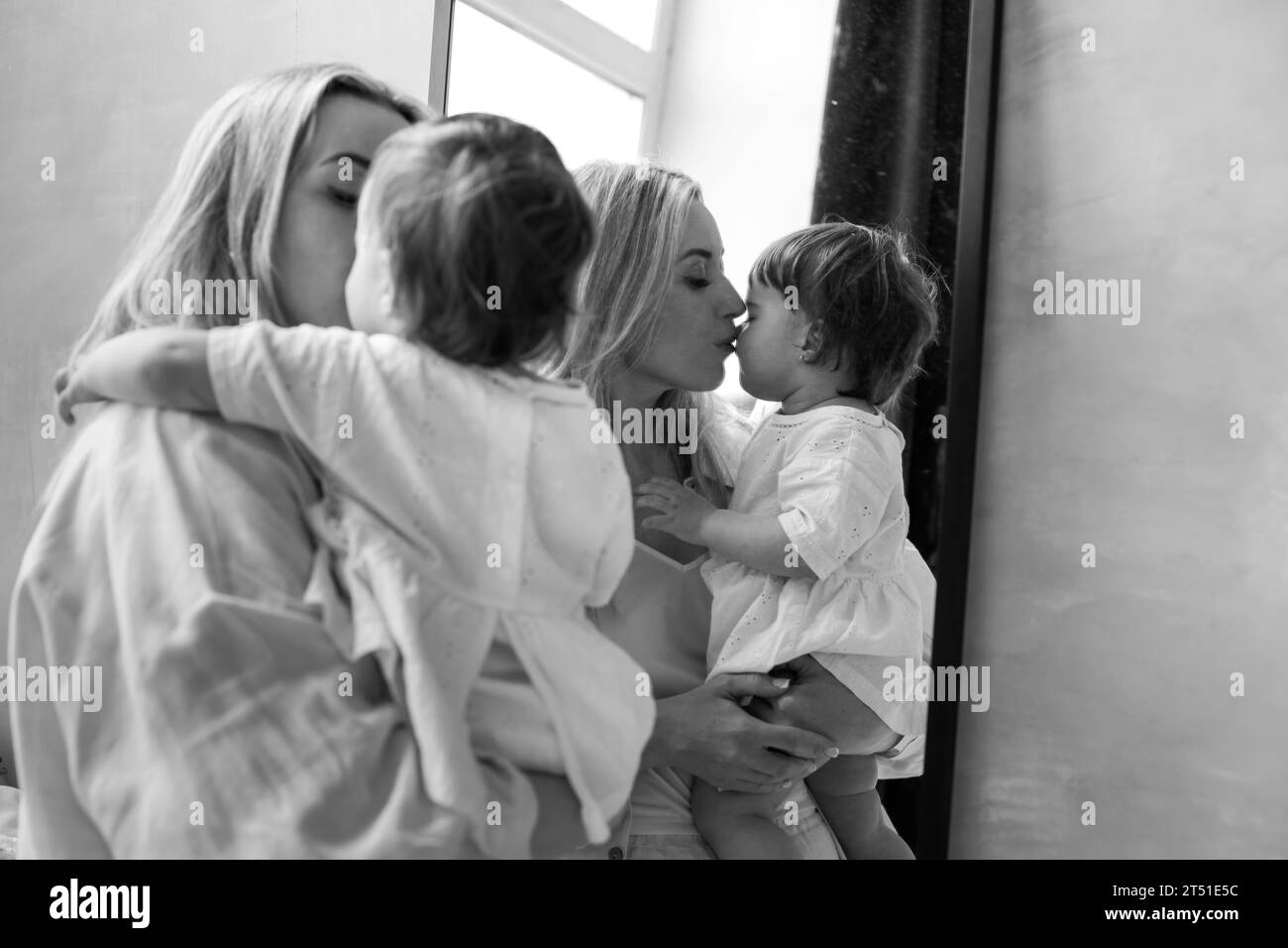 Familienporträt. Eine Mutter steht am Spiegel mit ihrer einjährigen Tochter im Arm, die Mutter umarmt und küsst ihre Tochter. Sie spiegeln sich wider Stockfoto