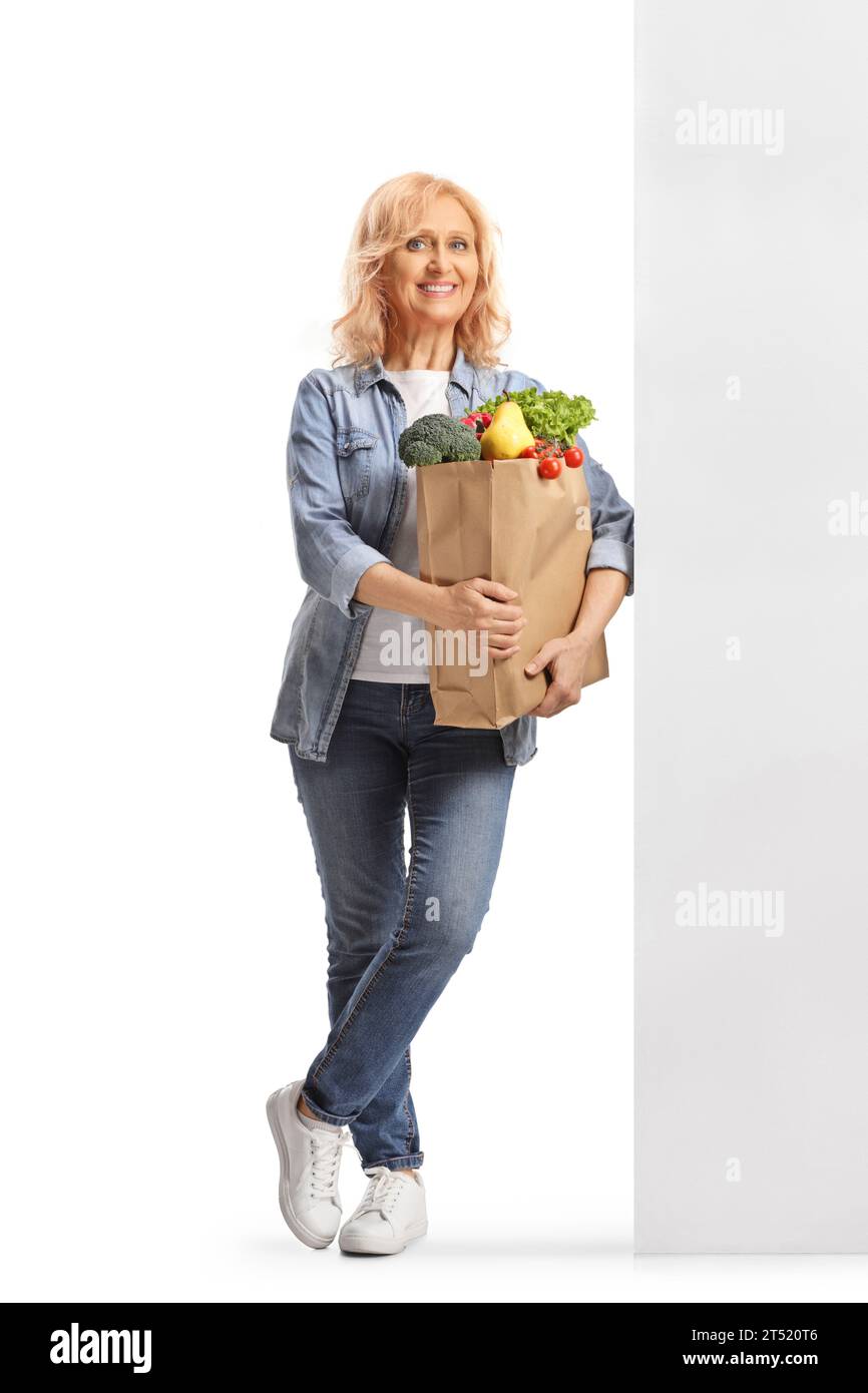 Porträt einer Reifen Frau mit einer Lebensmitteltasche, die an einer Wand steht und auf weißem Hintergrund lächelnd Stockfoto