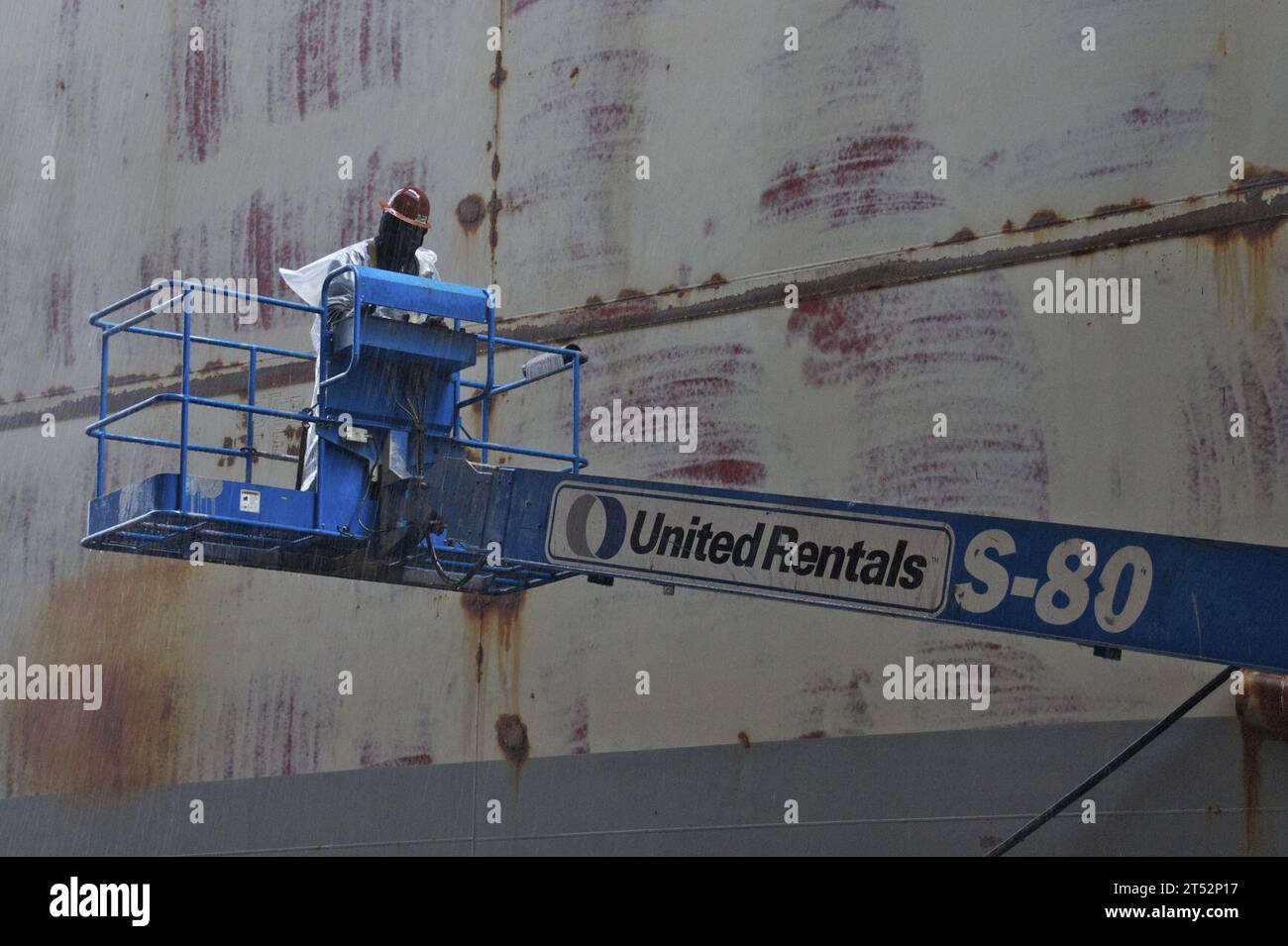 1012219643K-452 SAN DIEGO (21. Dezember 2010) Ein Arbeiter der NASSCO-Werft arbeitet mit einem Lift weiter am Rumpf des amphibischen Angriffsschiffs USS Bonhomme Richard (LHD 6), obwohl es mehrere Tage lang regnet. Bonhomme Richard befindet sich im Trockendock für Wartungsarbeiten und Upgrades. Marineblau Stockfoto