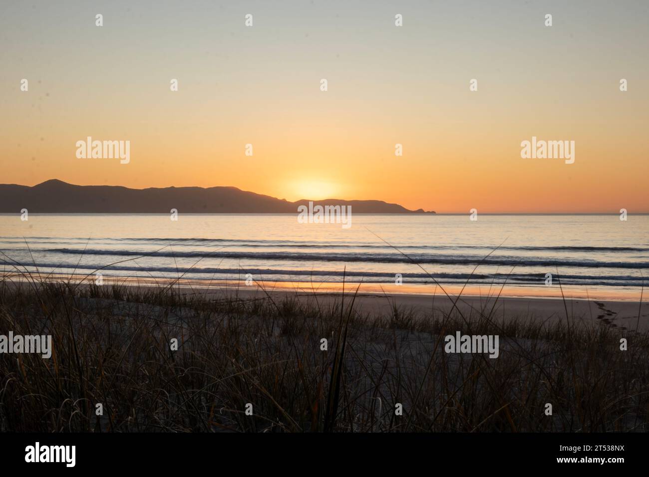 Golden Hour Serenity: Die Golden Sun taucht unter dem Horizont mit Wasser im Vordergrund bei Sonnenuntergang über der neuseeländischen Küste der Spirits Bay Stockfoto