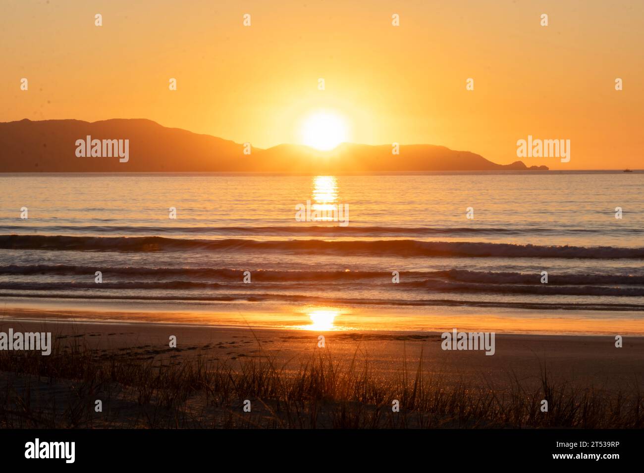 Golden Hour Serenity: Die Golden Sun taucht unter dem Horizont mit Wasser im Vordergrund bei Sonnenuntergang über der neuseeländischen Küste der Spirits Bay Stockfoto