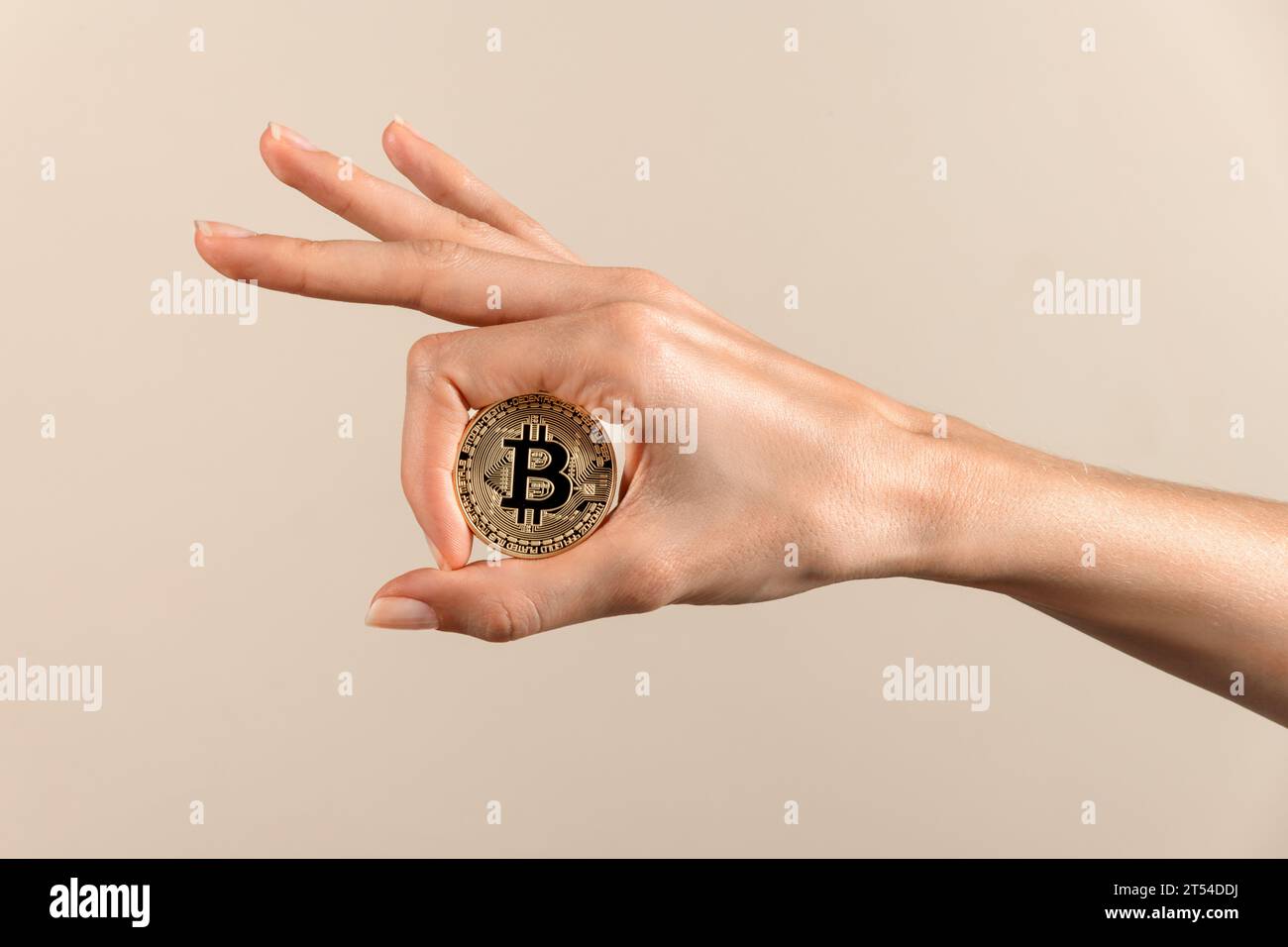 Anonyme Frau mit rundem Bitcoin mit B-Inschrift in der Mitte mit gepflegtem Daumen und Zeigefingern der Hand in reflektierendem Licht gegen beige bac Stockfoto