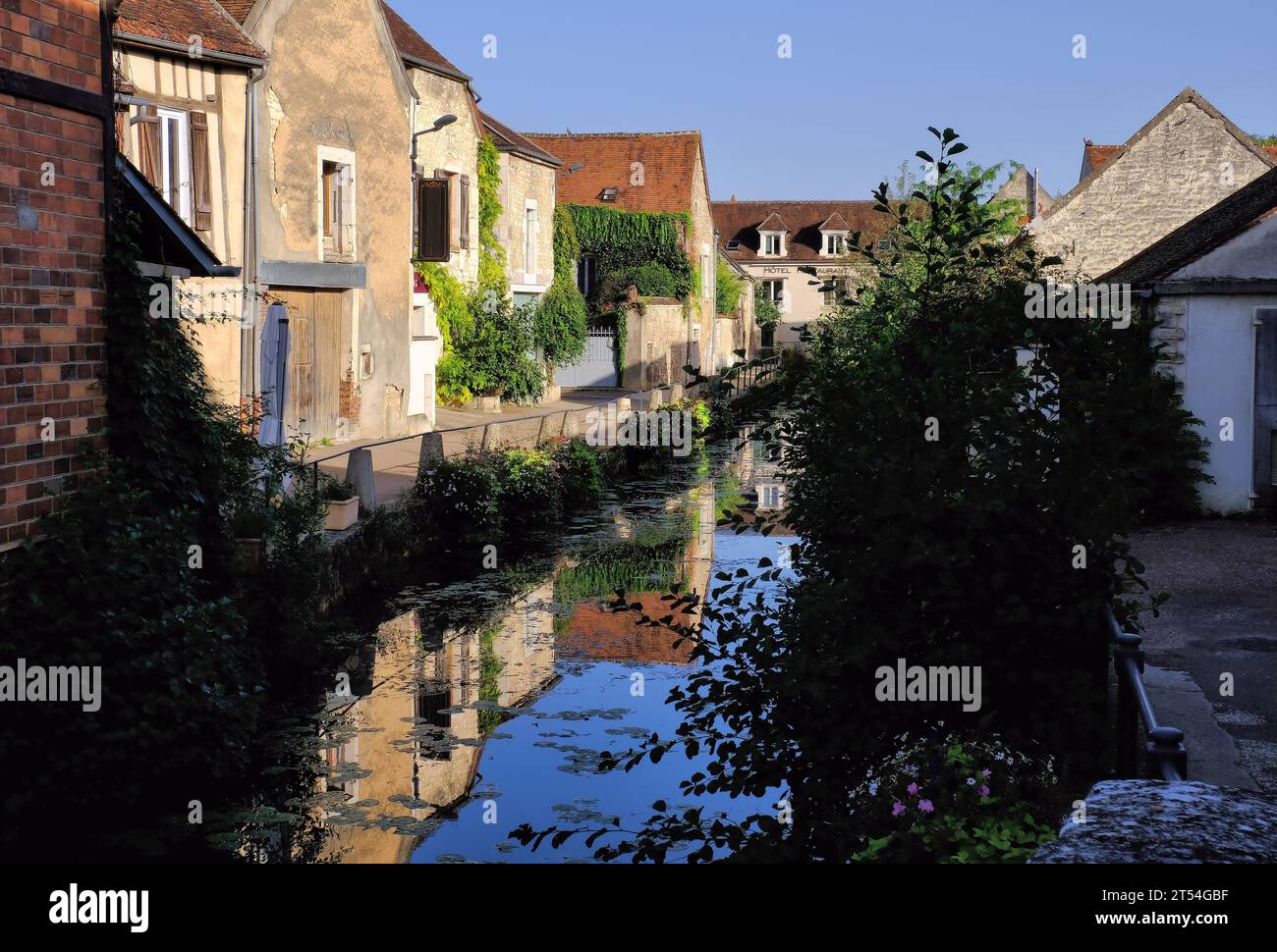 Chablis: Ehemalige Mühle (heute Hotel) und andere Gebäude mit Spiegelreflexen im Fluss Serein kurz nach Sonnenaufgang in Chablis, Burgund, Frankreich Stockfoto