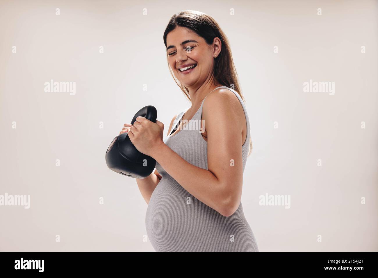 Schwangere Frau im dritten Trimenon hebt eine Kettlebell in einem gut ausgestatteten Fitnessstudio. Sie legt Wert auf ihr Wohlbefinden und nähert sich der Mutterschaft Stockfoto