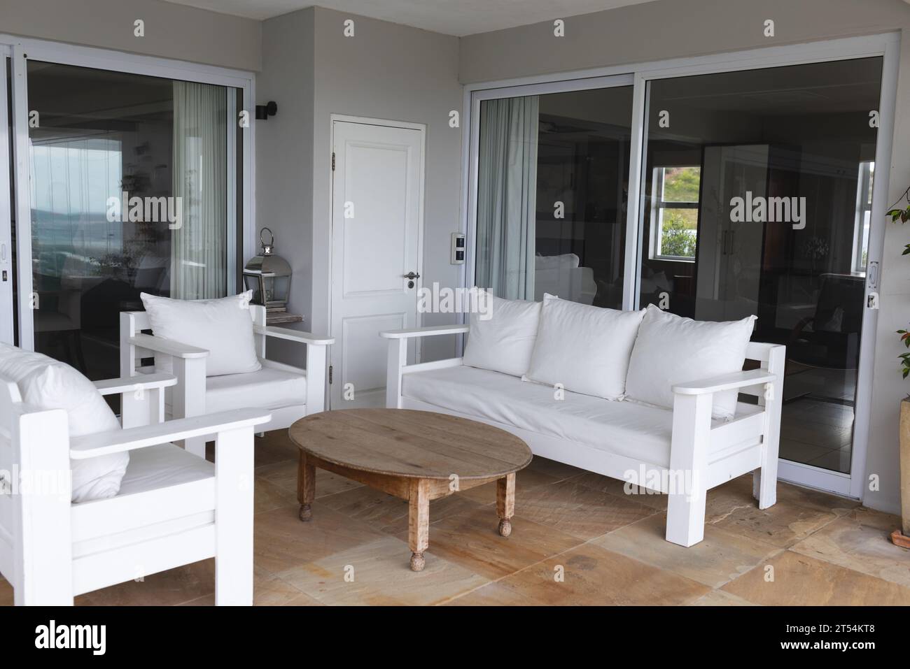 Leeres großes graues Wohnzimmer mit weißer Couch, Stühlen, Kissen und großen Fenstern Stockfoto