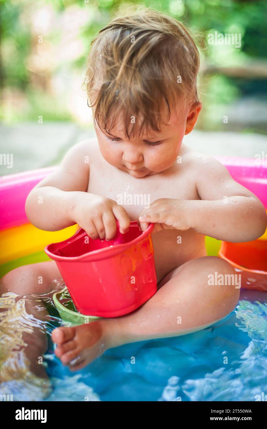 Ein süßer kleiner Junge spielt mit Spielzeug, während er in einem kleinen farbenfrohen Planschbecken badet. Sommerzeit. Freude und Glück Konzept. Liebe und Familie Stockfoto