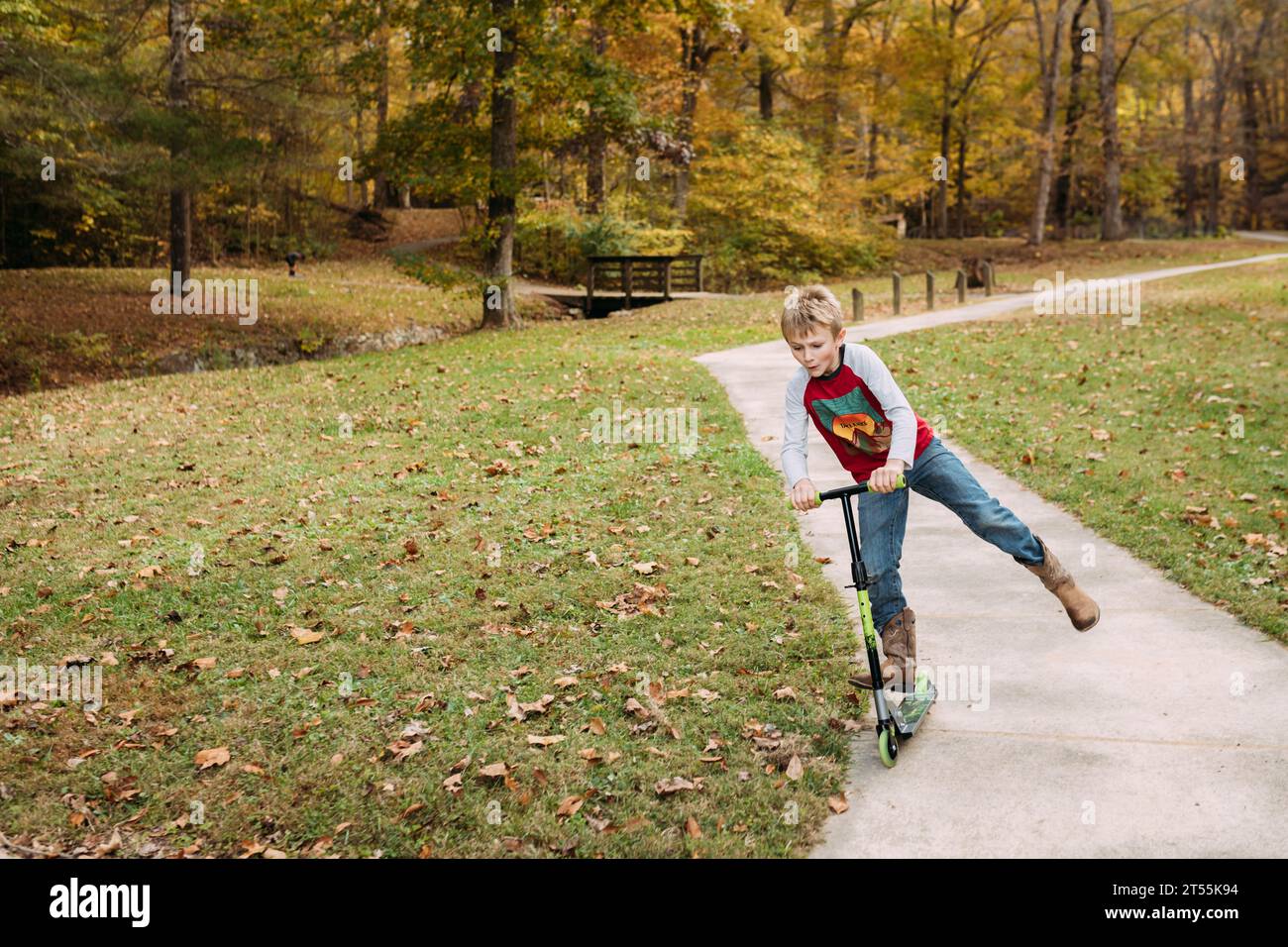 Junge, der im Herbst auf dem Bürgersteig in einem Park fährt Stockfoto