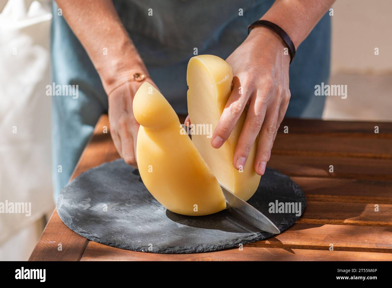 Weibliche Hand schneidet einen Caciocavallo silano Käse auf einem Schneidebrett Stockfoto