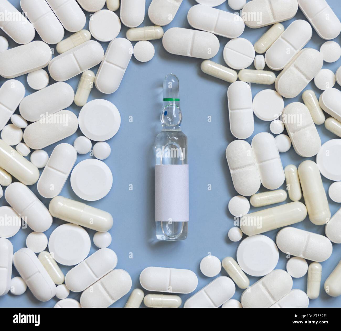 Mischung aus weißen medizinischen Kapseln und Pillen mit Ampulle in der Mitte auf hellblauer Draufsicht. Medikamentöse Behandlung. Verschiedene pharmazeutische Produkte Stockfoto