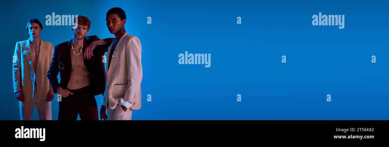 Interrassische männliche Models in lebendigen Anzügen, die sich in Neonlichtern ausgeben, Kamera, Männer-Power, Banner ansehen Stockfoto