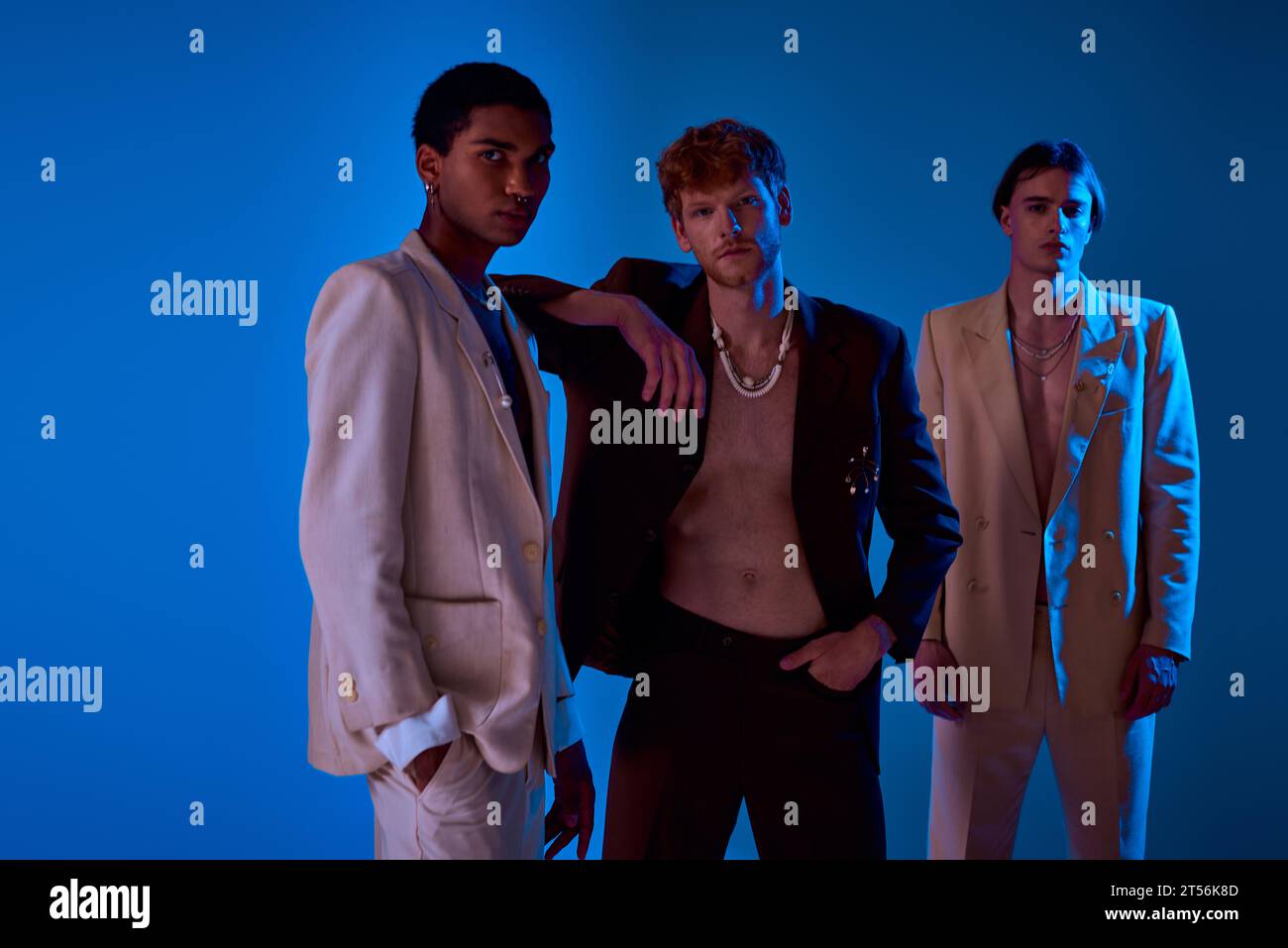 Drei multikulturelle männliche Models in lebendigen Anzügen, die sich in Neonlichtern ausgeben, die Kamera betrachten, die Macht der Männer Stockfoto