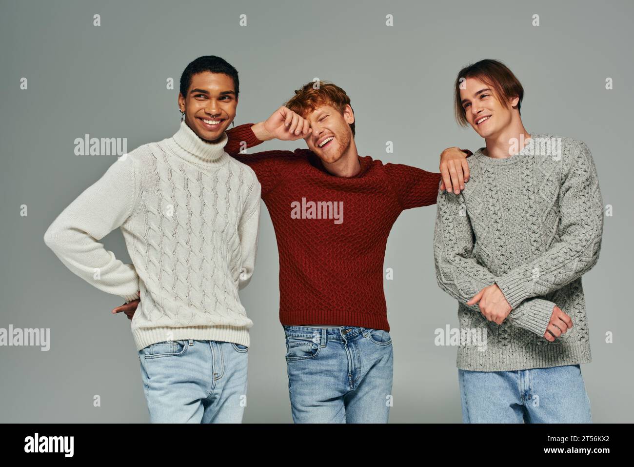 Fröhliche verschiedene männliche Models in lässigen Pullover, lachen und posieren vor grauem Hintergrund, Männer Power Stockfoto