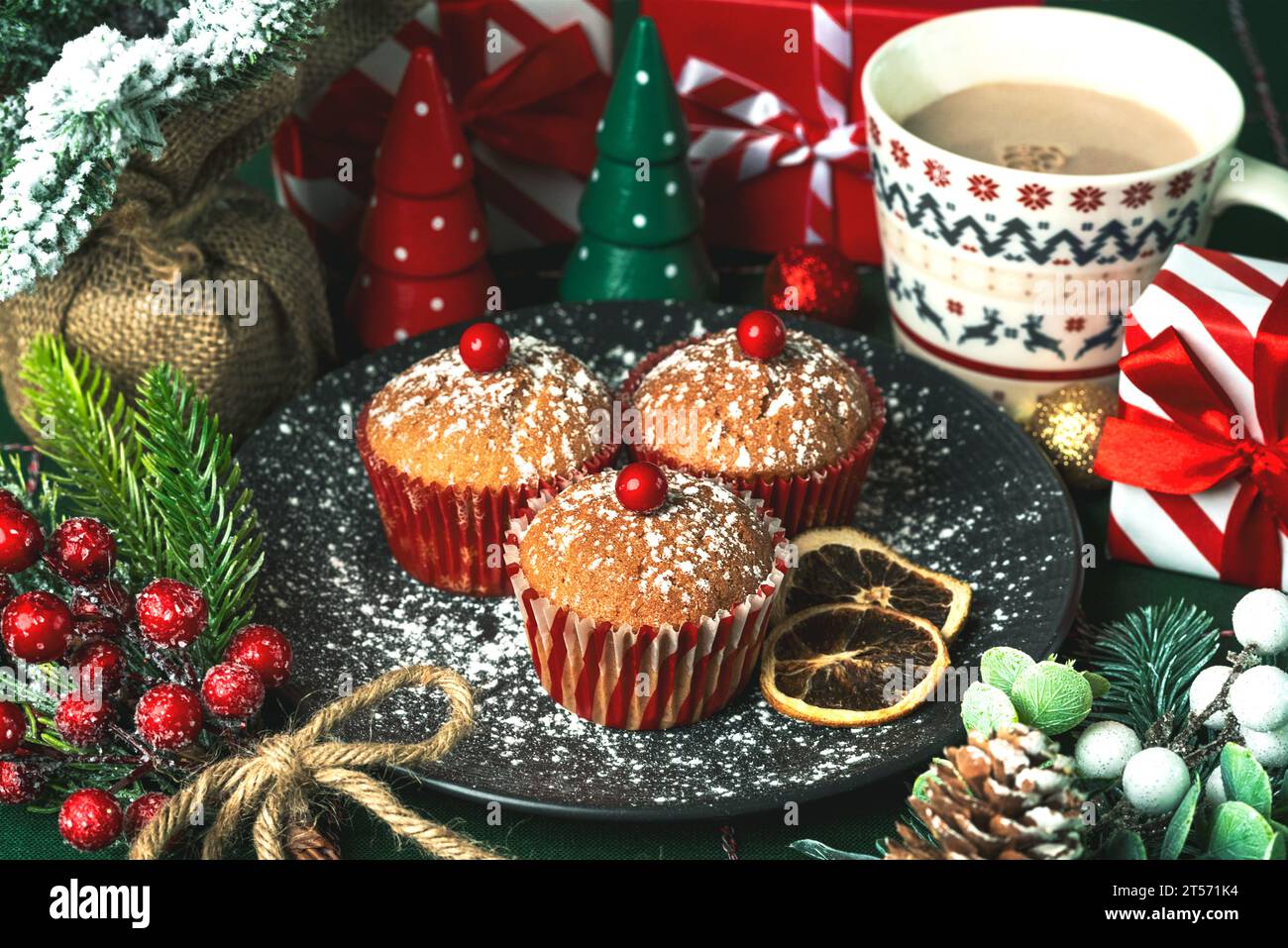 Hausgemachte weihnachtsmuffins mit roter Kirsche und weihnachtsdekoration auf einer weihnachtstischdecke. Weihnachtliches süßes Konzept Stockfoto