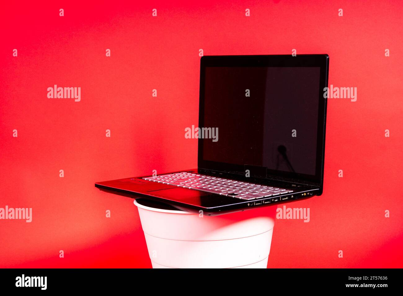 Schwarzer Laptop in einem Papierkorb auf rotem Hintergrund isoliert Stockfoto